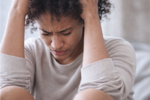 Woman holding her head with eyes closed, appearing overwhelmed by PTSD Intrusive Symptoms and trauma-related stress.